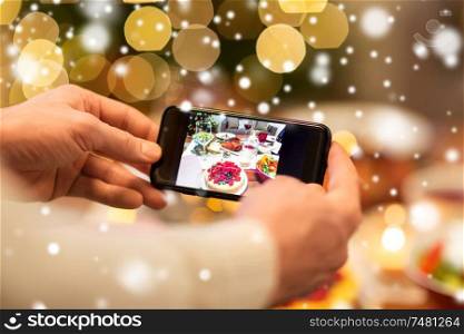 food, technology and holidays concept - close up of male hands photographing cake by smartphone at christmas dinner over snow. hands photographing food at christmas dinner