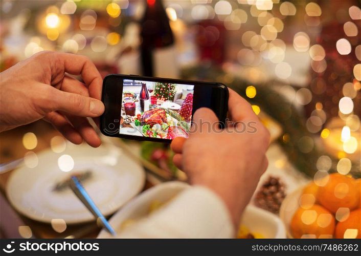 food, technology and holidays concept - close up of male hands photographing roast turkey by smartphone at christmas dinner. hands photographing food at christmas dinner