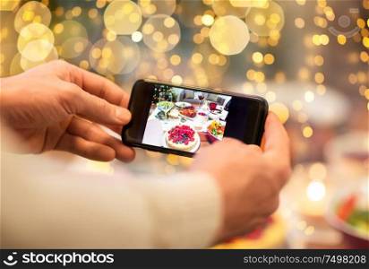 food, technology and holidays concept - close up of male hands photographing cake by smartphone at christmas dinner. hands photographing food at christmas dinner