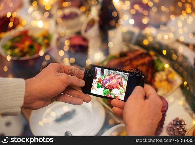 food, technology and holidays concept - close up of male hands photographing roast turkey by smartphone at christmas dinner. hands photographing food at christmas dinner