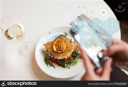 food, technology, eating and people concept - woman with smartphone, breaded fish fillet and nutritional value chart at restaurant. hands with phone and food nutritional value chart