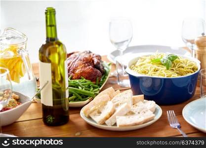 food, thanksgiving day and eating concept - bottle of wine with bread, pasta and roast chicken on served wooden table. bottle of wine and food on served wooden table