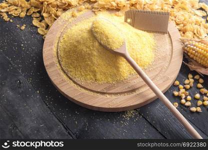 Food theme image with corn flour on a round wooden board and a spoon, with a blank etiquette, surrounded by corn flakes and grains, on a rustic black table.