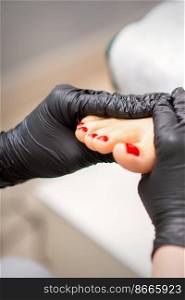 Foot massage with moisturizing and peeling cream by pedicurist hands wearing black gloves, close up. Foot massage with moisturizing and peeling cream by pedicurist hands wearing black gloves, close up.