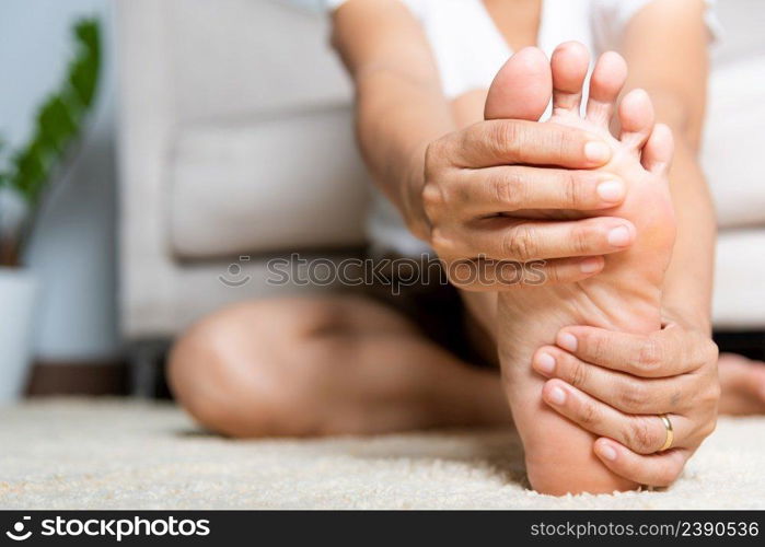 Foot pain, Asian woman feeling pain in her foot at home, female suffering from feet ache use hand massage relax muscle from soles in home interior, Healthcare problems and podiatry medical concept