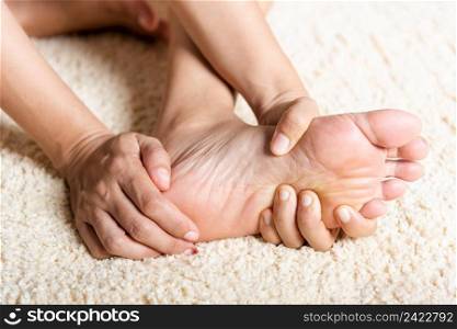 Foot pain, Asian woman feeling pain in her foot at home, female suffering from feet ache use hand massage relax muscle from soles in home interior, Healthcare problems and podiatry medical concept
