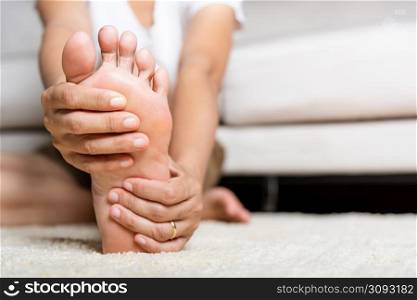Foot pain, Asian woman feeling pain in her foot at home, female suffering from feet ache use hand massage relax muscle from soles in home interior, Healthcare problems and podiatry medical concept