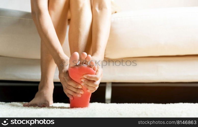 Foot pain, Asian woman sitting on sofa feeling pain in her foot at home, female suffering from feet ache use hand massage relax muscle from soles in home interior, Healthcare and podiatry medical