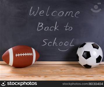 Football and soccer ball on desktop. Erased black chalkboard in background along with welcome back to school message to students.
