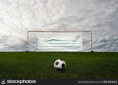 football competitions restart after the coronavirus pandemic.new league season and COVID-19 concept. medical face mask on goal post and soccer ball on the green grass.