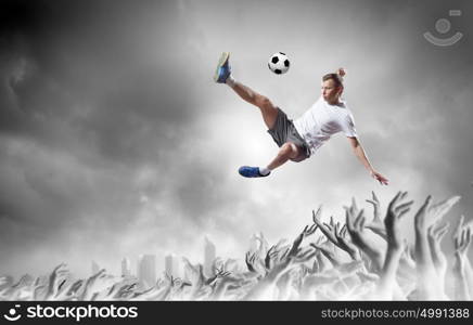 Football fans. Football player in jump kicking the ball supported by fans