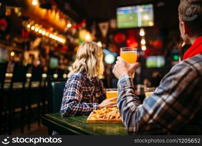 Football fans watching match and drinks beer at the table in sports bar. Tv broadcasting, young friends leisures in the pub. Fans watching match and drinks beer in sports bar