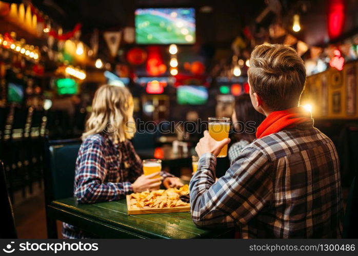 Football fans watching match and drinks beer at the table in sports bar. Tv broadcasting, young friends leisures in pub
