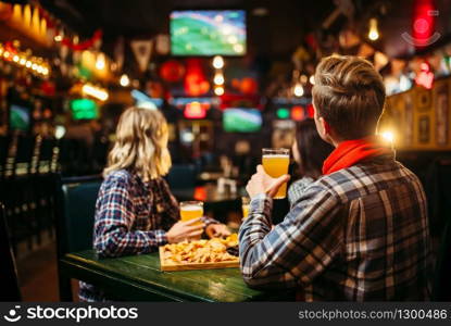 Football fans watching match and drinks beer at the table in sports bar. Tv broadcasting, young friends leisures in pub