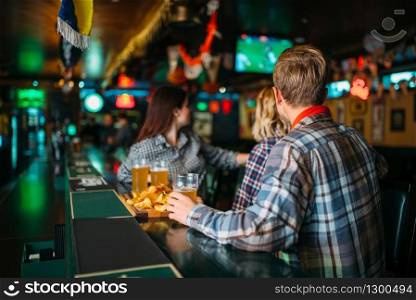 Football fans with glasses of beer at the counter in sports bar. Tv broadcasting, young friends celebrates win of the favorite team, success game celebration in pub. Fans with glasses of beer at counter in sports bar