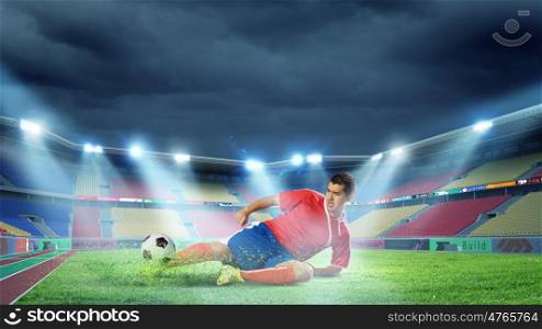Football kick. Football player at stadium sliding to kick the ball