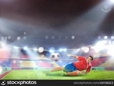 Football kick. Football player at stadium sliding to kick the ball