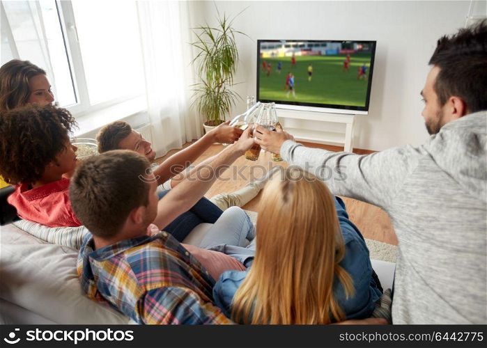 football, leisure and people concept - happy friends clinking beer bottles and watching soccer game on tv at home. friends clinking beer and watching soccer game