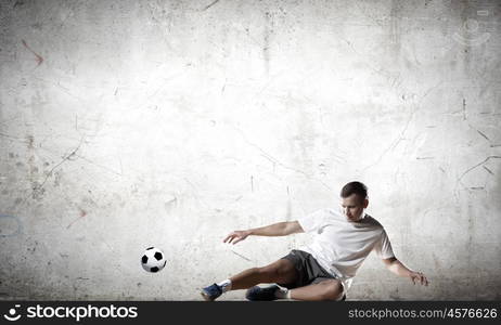 Football player. Football player kicking ball against cement background