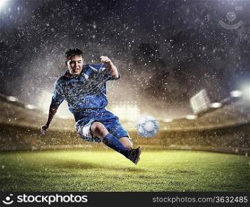 football player in blue shirt striking the ball aloft at the stadium under the rain