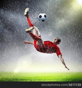 football player in red shirt striking the ball at the stadium under rain