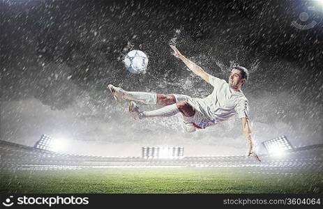 football player in white shirt striking the ball at the stadium under rain