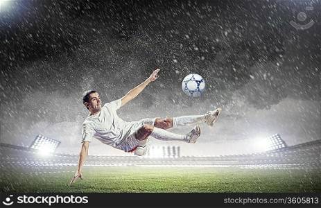 football player in white shirt striking the ball at the stadium under rain