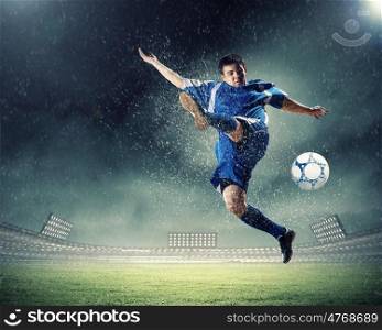 football player striking the ball. football player in blue shirt striking the ball aloft at the stadium under the rain