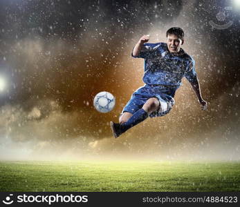 football player striking the ball. football player in blue shirt striking the ball aloft at the stadium under the rain