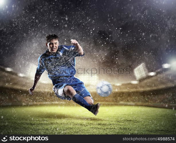 football player striking the ball. football player in blue shirt striking the ball aloft at the stadium under the rain