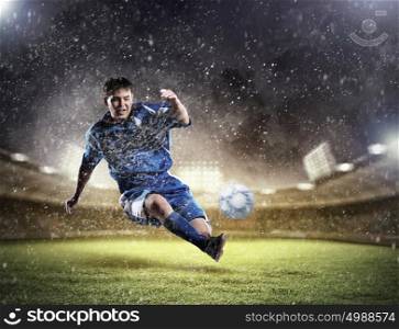 football player striking the ball. football player in blue shirt striking the ball aloft at the stadium under the rain