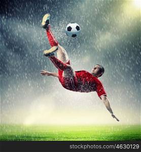football player striking the ball. football player in red shirt striking the ball at the stadium under rain
