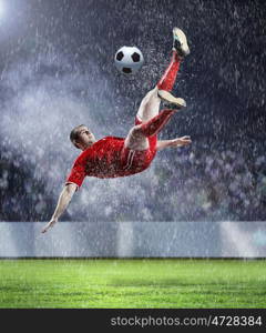 football player striking the ball. football player in red shirt striking the ball at the stadium under rain