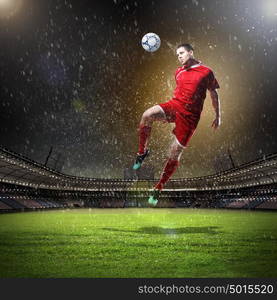 football player striking the ball. football player in red shirt striking the ball at the stadium under rain