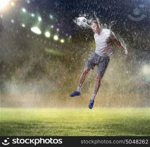 football player striking the ball. football player in white shirt striking the ball with head at the stadium under the rain