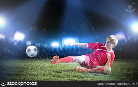 Football player. Young football player on stadium doing slide tackle