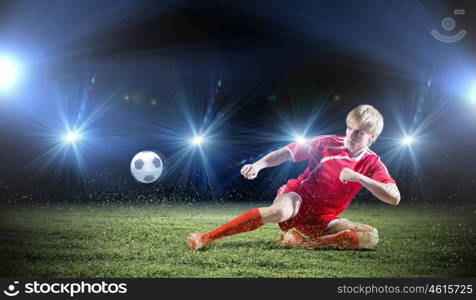 Football player. Young football player on stadium doing slide tackle