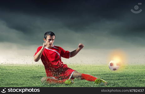 Football player. Young football player on stadium doing slide tackle