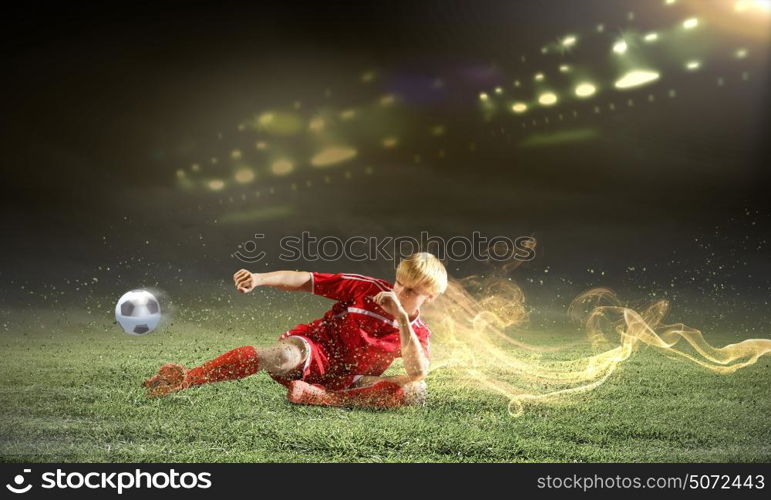 Football player. Young football player on stadium doing slide tackle