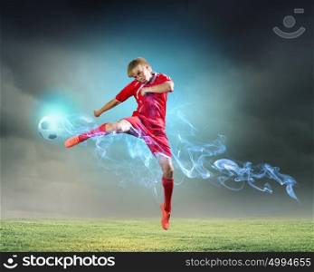 Football player. Young football player on stadium kicking ball in jump