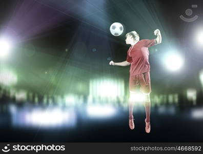 Football player. Young football player on stadium kicking ball with head in jump