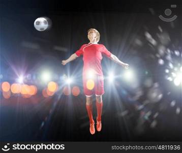 Football player. Young football player on stadium kicking ball with head in jump