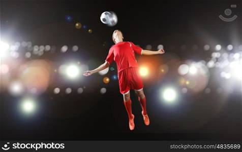 Football player. Young football player on stadium kicking ball with head in jump