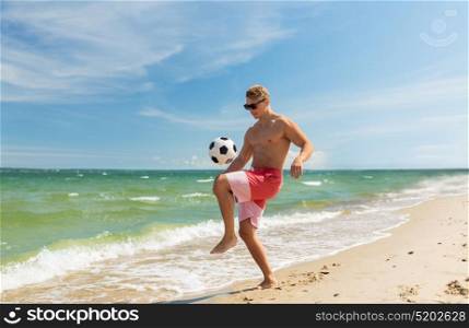 football, sport, fitness and people concept - young man with ball playing soccer on summer beach. young man with ball playing soccer on beach