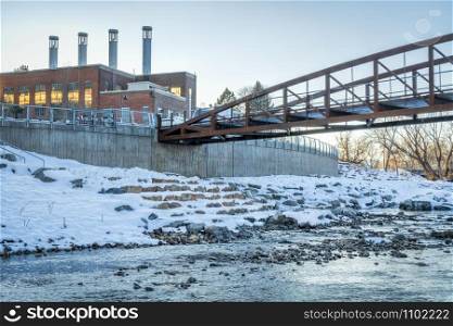 footbridge over Cache la Poudre River at newly developed whitewater park in downtown of Fort Collins Colorado with Powerhouse Energy Campus of Colorado State University in background, winter sunset scenery