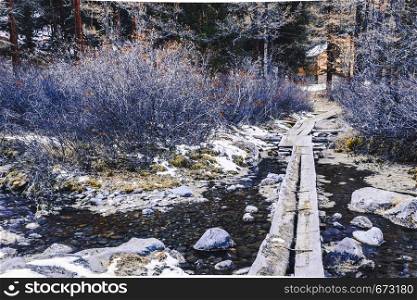 Footpath in forest over mountain stream. Bridge of boards under snow