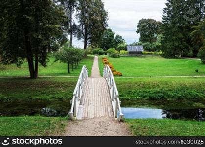 Footpath with white wooden bridge in old park of the village Mikhailovskoye, Pushkinskiye Gory Reserve, Russia