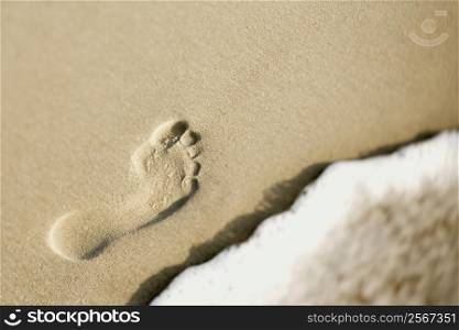 Footprint in sand next to wave.