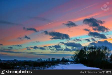 Footprints in the snow and silhouettes of trees against the background of a dramatic cloudy sky with pink wide strips at sunset . Selective focus.. Winter Landscape With Pink Clouds At Sunset