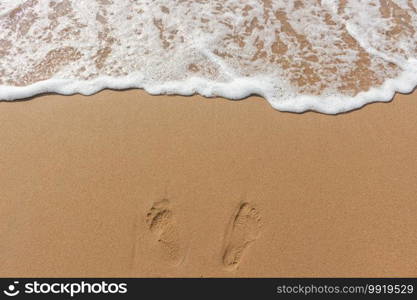 Footprints on the sand of the beach and white color of sea wave bubble